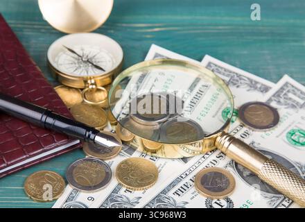Concetto finanziario. Notebook in pelle, stilografica, lente d'ingrandimento, monete e bussola su un tavolo in legno verde. Foto Stock