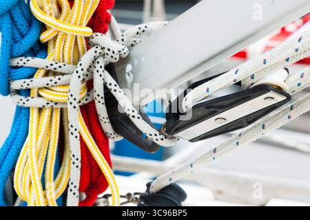Corde di ricambio multicolore legate all'albero di una nave a vela, primo piano. Una fune è fissata sui rulli di fissaggio sull'albero della barca a vela. Foto Stock