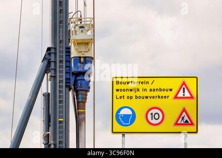 Cartello con la scritta olandese "cantiere - zona residenziale in costruzione - attenzione al traffico" davanti all'attrezzatura di costruzione Foto Stock