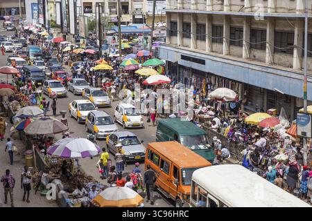 Accra, Ghana - 27 maggio 2017: Vista di una vivace scena di strada, un vivace arazzo di ombrelli colorati, taxi gialli e persone vicino al mercato di Makola, vive di commercio e movimento. Foto Stock