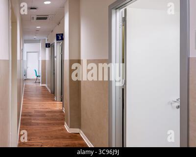Corridoio di una clinica medica con vista sulle porte numerate degli uffici medici, pavimento in parquet e pareti marroni. Foto Stock