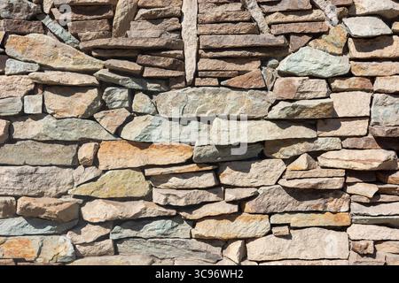 Primo piano di una parete di pietra intemprata, che mostra un'intricata disposizione di rocce colorate e stratificate, evocando un senso di storia e consistenza. Foto Stock