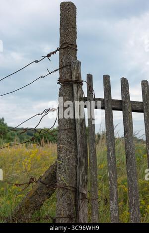 Una vecchia recinzione con filo spinato contro un cielo nuvoloso. Una scena rurale rustica. Foto Stock