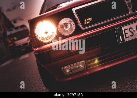 Roma, italia 5 agosto 2025: Primo piano di un delta rosso della lancia integrale evo, fari che illuminano una strada della città al crepuscolo Foto Stock