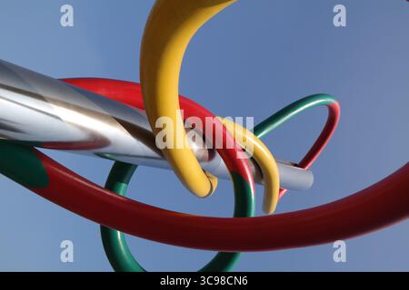 Un'immagine a basso angolo di una scultura d'arte moderna realizzata con anelli in metallo dai colori vivaci intrecciati intorno a un pezzo centrale in metallo lucido Foto Stock