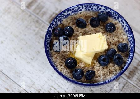Ciotola di farina d'avena con mirtilli e burro su fondo di legno Foto Stock