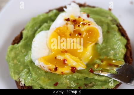 Toast all'avocado con uovo in camicia su un piatto bianco, primo piano Foto Stock