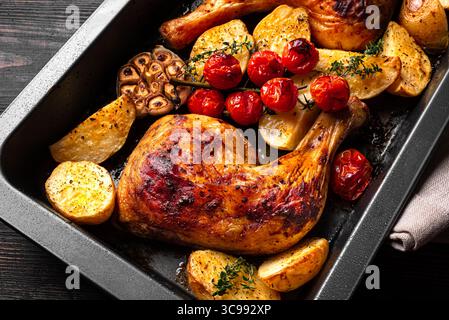 Cosce di pollo arrosto al forno con patate, pomodori, aglio ed erbe aromatiche in teglia da forno. Abbondante pasto fatto in casa - pollo e verdure. Foto Stock