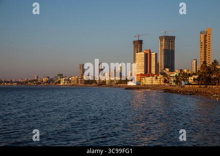 Moderno skyline cittadino di Mumbai con alti edifici e grattacieli lungo la costa, bagnato dalla calda luce del sole serale con mare calmo in primo piano Foto Stock