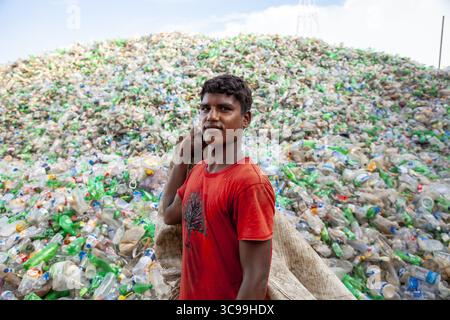 Chittagong, Bangladesh - 22 settembre 2022: Veduta di un giovane uomo in piedi davanti a una montagna torreggiante di bottiglie di plastica scartate, che riflettono la resilienza. Foto Stock
