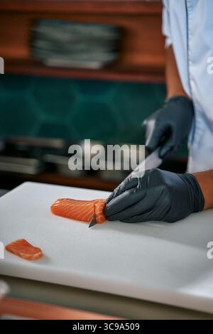Chef esperto che affetta meticolosamente filetto di salmone fresco con coltello di precisione su tagliere pulito in un ambiente moderno Foto Stock