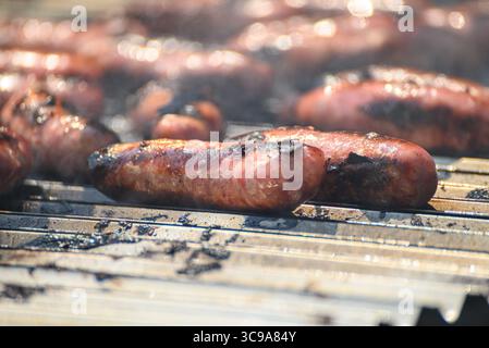 Salsicce sfrigolanti su una griglia calda con affumicatura. Grigliare la carne su una griglia calda. Foto Stock