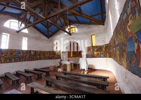 Kalacha, Kenya - 12 maggio 2022: Veduta dell'interno di una chiesa, dove la luce del sole scorre attraverso le finestre, illuminando i murales che fiancheggiano le pareti e le semplici panche di legno. Foto Stock