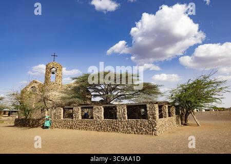 Kalacha, Kenya - 12 maggio 2022: Veduta della chiesa di pietra sotto un cielo blu luminoso punteggiato da soffici nuvole bianche, una testimonianza della fede e della resilienza Foto Stock