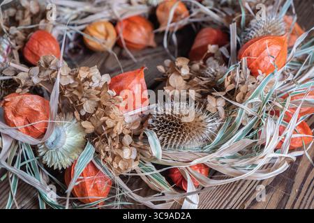 Primo piano della corona floreale essiccata da materiali naturali su fondo di legno scuro. Decorazioni autunnali. Concetto del Ringraziamento Foto Stock
