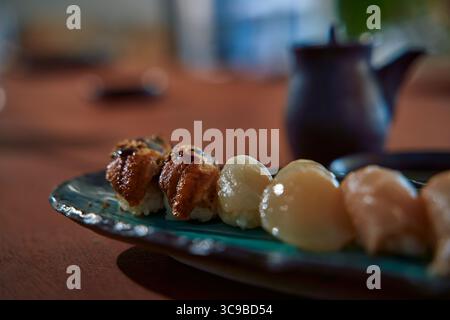 Una vista ravvicinata dello squisito sushi caratterizzato da pesce alla griglia e delicati frutti di mare su un piatto splendidamente disposto circondato da un'atmosfera calda Foto Stock