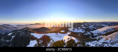 Vista aerea delle coperte di neve baciate dal sole sulle colline ondulate, che gettano lunghe ombre sul paesaggio delle meraviglie invernali dell'Almenland, Sommeralm, Steiermark, Austria. Foto Stock