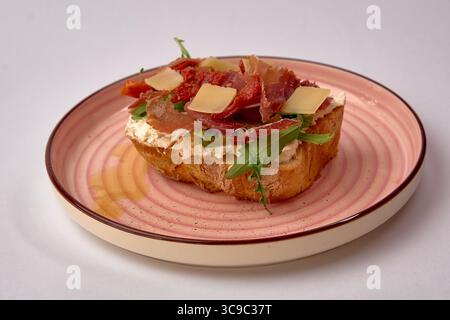 Delizioso panino aperto con prosciutto salato, rucola fresca e formaggio cremoso su una fetta rustica di pane Foto Stock