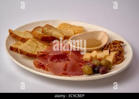 Un piatto ben organizzato con prosciutto a fette, formaggio, noci, olive, frutta secca, e pane croccante per un'esperienza gourmet Foto Stock