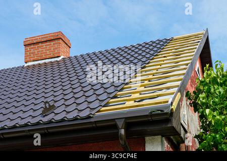 Vista ravvicinata di un'installazione del tetto in corso con piastrelle metalliche e camino su una casa, mostrando listelli di legno Foto Stock