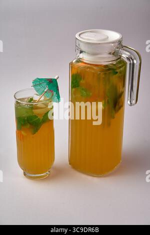 Bevanda rinfrescante agli agrumi servita in una caraffa e bicchiere con foglie di menta e ombrello colorato per un'esperienza estiva vivace Foto Stock