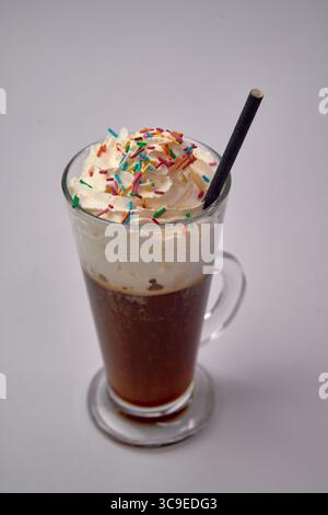Bevanda di caffè deliziosamente cremosa con panna montata e colorate goccioline in un bicchiere alto con cannuccia Foto Stock