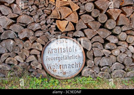 Fusto originale della Wehrmacht della seconda guerra mondiale parzialmente nascosto dietro la legna da ardere impilata nell'Estonia rurale, che mostra testo tedesco e superficie metallica arrugginita Foto Stock