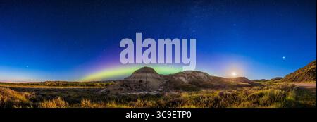 18 agosto 2022, Alberta, Canada: Questo cattura un panorama del cielo settentrionale sopra il paesaggio in primo piano del Dinosaur Provincial Park, Alberta, con la Luna che scende e un arco di aurora boreale sopra l'orizzonte settentrionale. Era previsto uno spettacolo Kp6 per questa notte, ma niente di spettacolare si è materializzato -- avevamo solo un arco quiescente attraverso il nord. ..questo avvenne la notte tra il 17 e il 18 agosto 2022. La Luna che sorge a destra è l'ultimo quarto di Luna. Giove è l'oggetto luminoso all'estrema destra. Il Big Dipper e l'Arcturus sono a sinistra; Polaris è in alto a sinistra nel centro; Cassiopea e Perseo Foto Stock