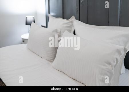Letto ben fatto con cuscini bianchi e lenzuola in una moderna camera d'hotel, simboleggia il comfort e la pulizia Foto Stock