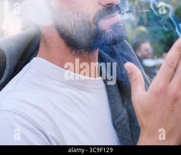 Primo piano della parte inferiore del volto dell'uomo che fuma nel centro della città europea, il volto è irriconoscibile Foto Stock