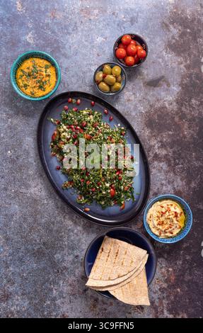Insalata di tabbouleh con hummus, salse, olive e focaccia. Un mezze vibrante e a misura d'istinto, disegnato su una superficie rustica. A base vegetale e fresca. Foto Stock