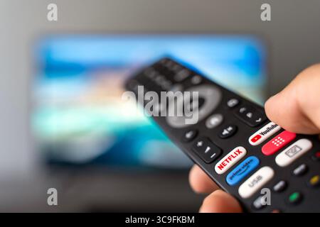 Tbilisi, Georgia - 2 luglio 2025: Foto ravvicinata di un telecomando smart TV con pulsanti dedicati per piattaforme di streaming popolari come Netflix, YouTube e Amazon prime, con uno schermo televisivo sfocato sullo sfondo. Rappresenta il consumo dei moderni media digitali, i servizi basati su abbonamento e l'intrattenimento on demand. Ideale per contenuti tecnologici, in streaming, binge-watching o media lifestyle. Foto Stock