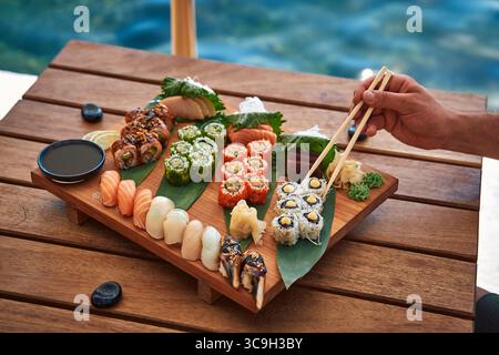Uno squisito piatto di sushi presentato ad arte su una tavola di legno, caratterizzato da diverse varietà, tra cui Maki, Sashimi e Rolls colorati con Dippi Foto Stock