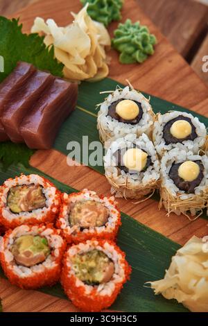 Un colorato piatto di sushi che mostra vari tipi di panini di sushi, pesce fresco, Wasabi e zenzero martellato su una tavola da servizio in legno Foto Stock