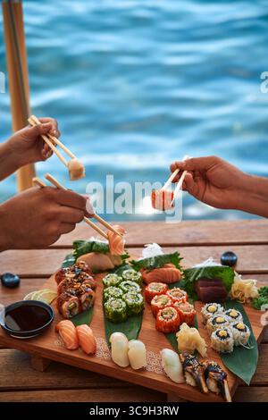 Assapora un delizioso sushi fresco sul bordo dell'acqua con le mani che tengono i bastoncini pronti a viziarti con ogni gusto Foto Stock