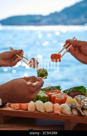 Gustatevi il fresco sushi sul lungomare: Una deliziosa esperienza di cucina Giapponese con Rolls colorati e Sashimi sotto la scintillante luce del sole Foto Stock