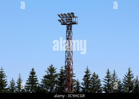 Una torreggiante struttura in metallo si erge sopra densa abete di abete picea abies, adagiata contro un cielo blu senza nuvole, mescolando tecnologia e natura Foto Stock