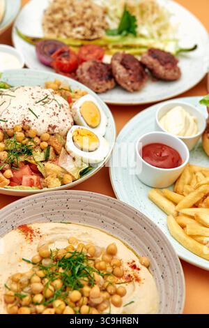 Una variopinta gamma di piatti mediterranei con insalate fresche, carni deliziose, cremose e patatine fritte in mezzo a ingredienti vivaci Foto Stock