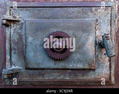 Porta della stufa in ghisa vintage con apertura a ingranaggi sul vecchio sito ferroviario, texture industriale e primo piano su patina. Foto Stock