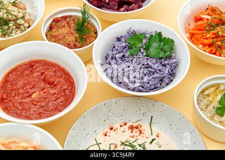 Una vivace gamma di piatti colorati esposti in ciotole con verdure fresche, salse cremose e salse salse salate su sfondo giallo Foto Stock