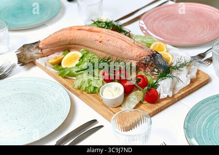 Un piatto di pesce splendidamente organizzato con un salmone intero guarnito con lattuga, pomodori, fette di limone e aneto, ideale per una cena festosa Foto Stock