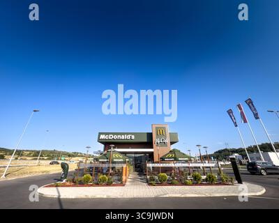 BELGRADO, SERBIA - 22 APRILE 2025: McDonald's con marchio McCafe e flagpole sotto un cielo azzurro. McDonald's è una catena americana di f Foto Stock