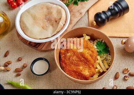 Un pasto deliziosamente placcato con cotolette di pollo croccanti, verdure fresche, Pane Pita e salsa piccante che eccita i sensi e stuzzica il gusto Foto Stock