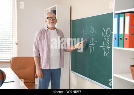 Insegnante maschile che conduce matematica vicino alla lavagna in classe Foto Stock