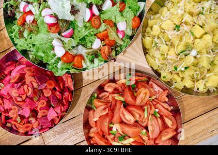 Una colorata gamma di insalate fresche con verdure, pomodori, ravanelli e patate, perfette per un pasto sano e vivace Foto Stock