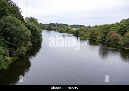 Vista panoramica di un ampio e tranquillo fiume che si snoda attraverso una lussureggiante foresta verde, presa da un ponte in una giornata nuvolosa. Foto Stock