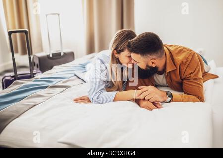 La giovane coppia felice è in vacanza. I turisti sono arrivati in camera d'albergo e si sono rilassati sul letto. Foto Stock