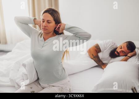 Una giovane coppia sta dormendo a letto. La donna si sta svegliando per lavoro. Foto Stock