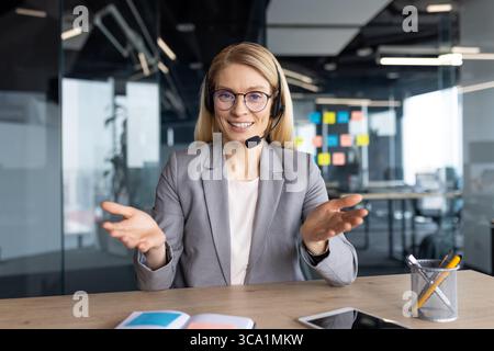 Un impiegato sorridente che indossa occhiali e cuffie sta parlando in un ufficio moderno. Foto Stock