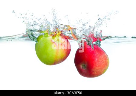 Mele dai colori vivaci che creano effetti di spruzzo in acqua cristallina, dando risalto alla freschezza. Foto Stock